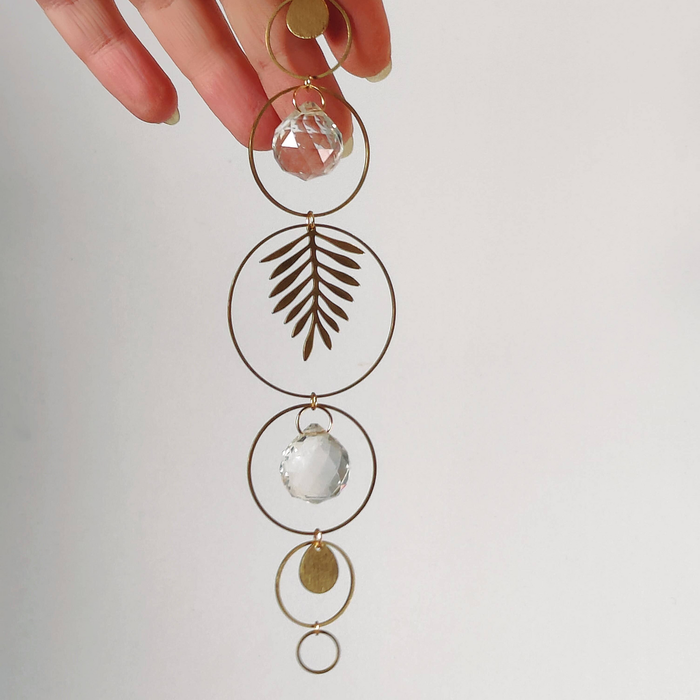 Messing suncatcher met cirkels, kristallen en messing blad, vastgehouden door een hand
